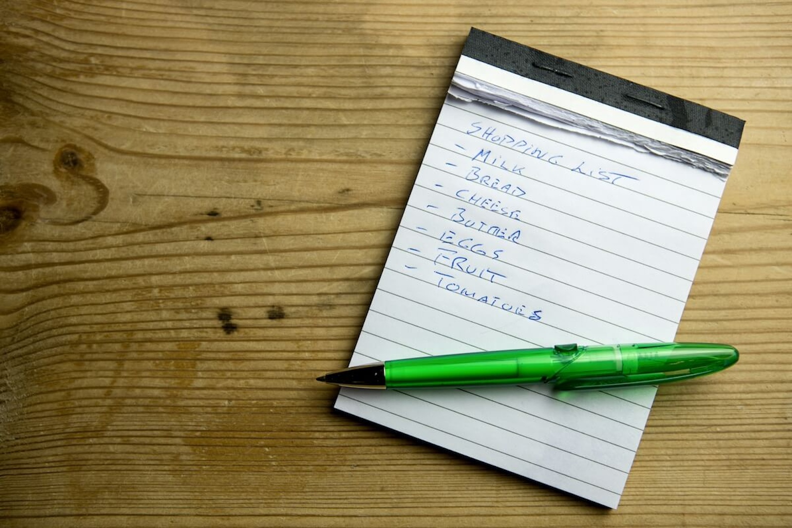 This image showcases a hand holding a mobile device with a shopping list displayed on a pink sticky note. The list includes essential grocery items, providing a relatable glimpse into the familiar task of preparing for a shopping trip. In context, it references the importance of grammar when making lists. 