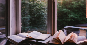 An open window overlooking a lush green forest, with books lying on the windowsill, creating a cozy and inviting atmosphere for reading.