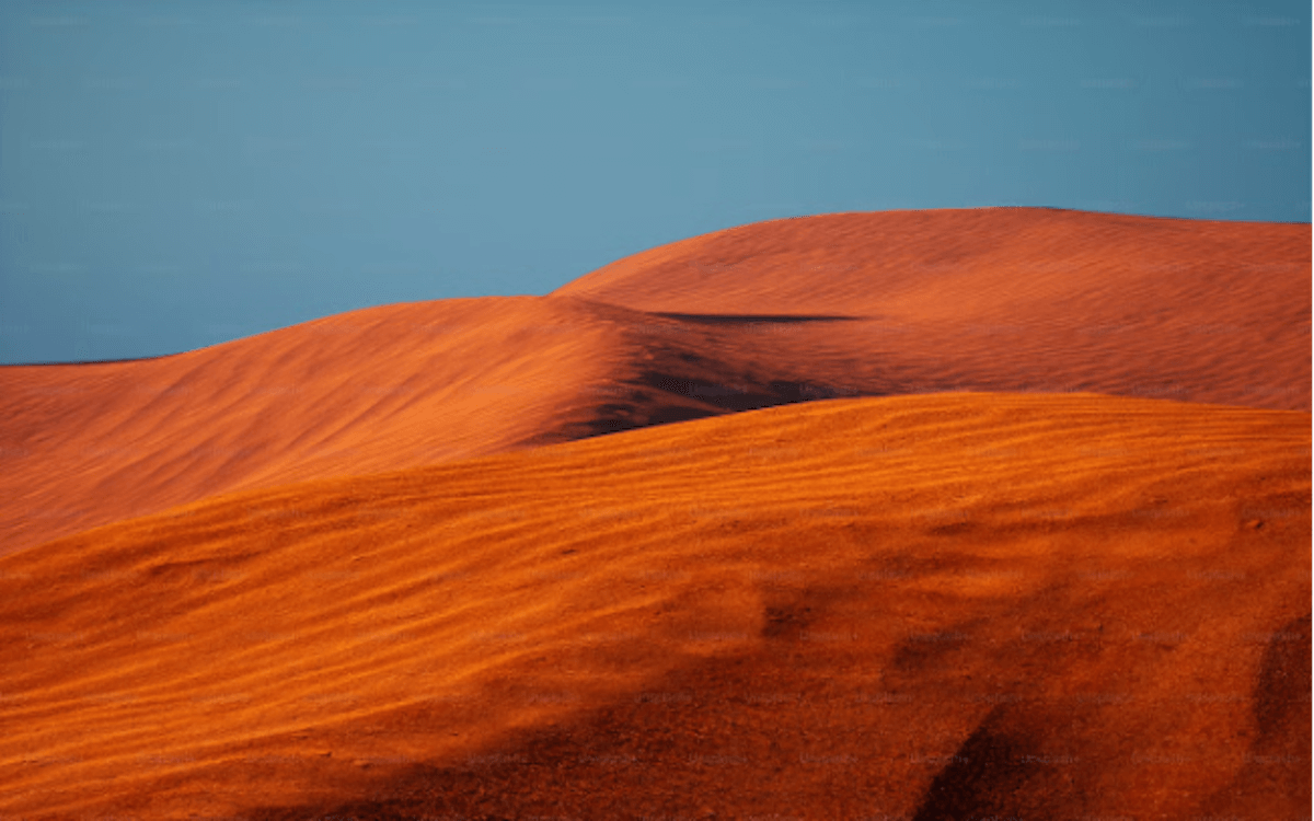 A vast, undulating landscape of orange sand dunes stretches out under a blue sky, evoking a sense of desolation and remoteness, representing Frank Herbert’s Dune series, a book that one might read if they ask themselves ‘what should I read next?’ 